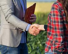 banker and farmer shaking hands in field